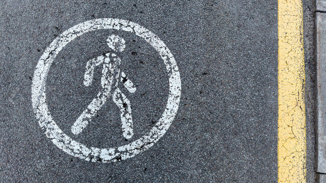 Pedestrian crossing symbol painted on asphalt with yellow safety line