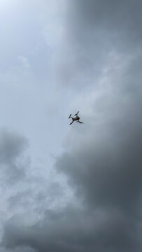 Small drone flying high in the overcast sky with dramatic clouds