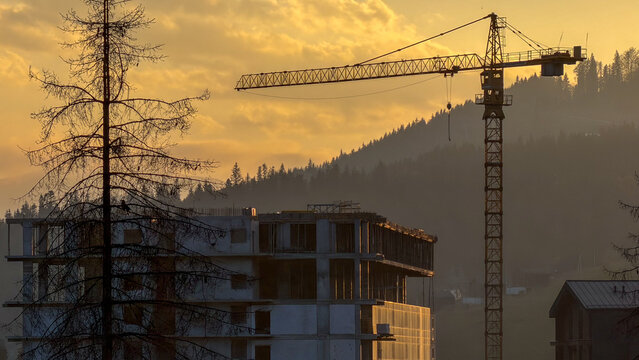 Construction crane silhouetted against a golden sunrise over a misty mountain landscape