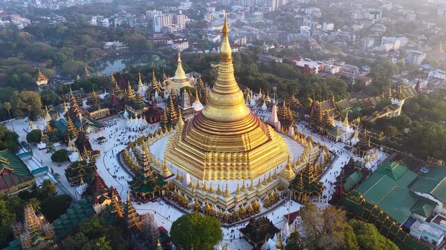 Aerial drone view at Shwedagon Pagoda, a golden stupa, surrounded by lush greenery and urban development in Yangon (Rangun), Myanmar (Burma), showcasing the city's blend of religious and modern life.