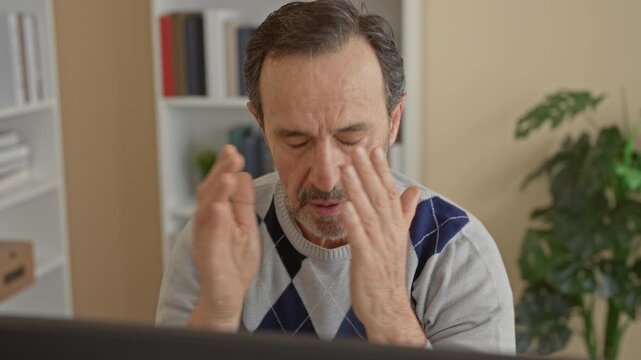 Man middle age hispanic at computer touching chin with hands and covering face gesture in building; fatigue overload.