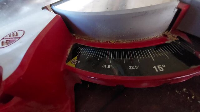 Hand adjusting the cutting angle degree scale on a red miter saw close up
