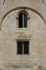 Fototapeta premium Historic limestone wall featuring a gothic arched window and a lower window with iron bars in Dubrovnik Old Town Croatia