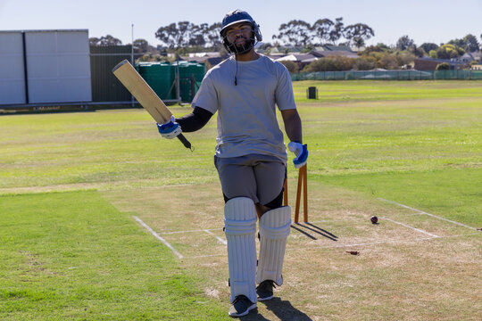 Cricket bat is resting beside stumps on prepared pitch, cricket ball is lying by crease
