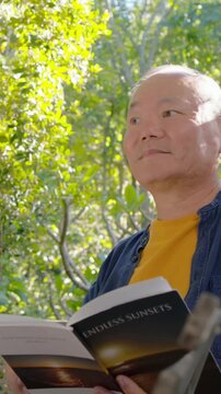 Vertical video: Pulling cam causing elder reading ENDLESS-SUNSETS on deck yellow shirt, copy space
