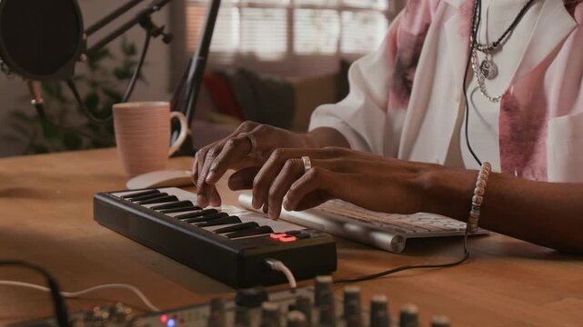 Close up shot on hands of unrecognizable Black male musician composing music on MIDI controller keyboard during recording session in home based music production studio