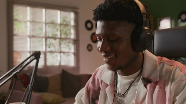 Tilt up shot of young adult African American male musician wearing headphones improvising on MIDI controller while recording electronic music in home based studio