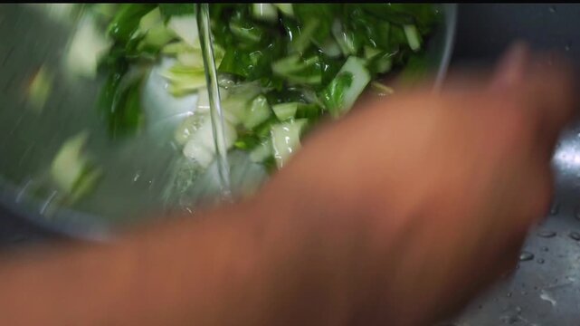 Close up of wet chopped green chard leaves draining in a metal colander inside a kitchen sink
