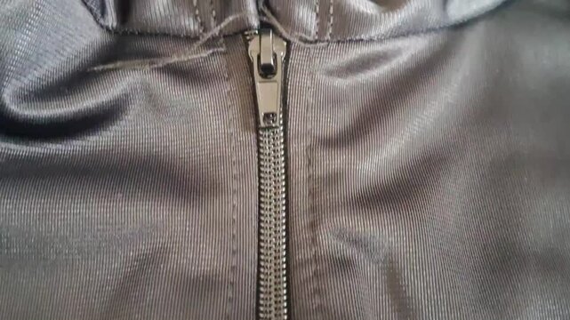 Metal zipper slider moving up along the fabric track on a dark grey sports jacket