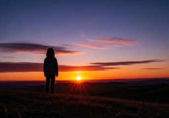 Obraz premium Little child standing on hill looking at picturesque sunset with colorful sky and clouds.