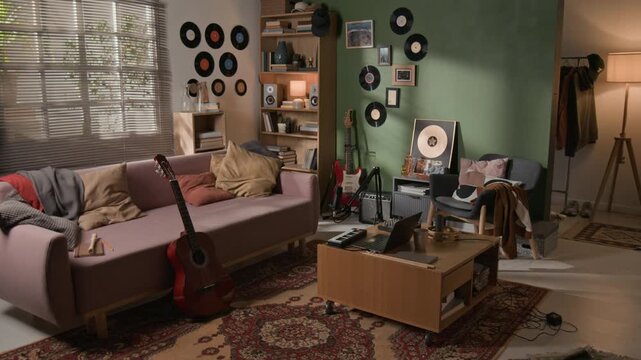 Wide shot of modern audio production workspace in apartment featuring laptop at workstation, cozy couch, professional microphone, electronic instruments for recording sessions