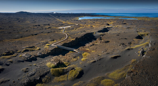 Aerial view of the Bridge Between Continents crossing a tectonic fissure in a vast volcanic landscape with dark lava fields and the ocean on the horizon Iceland.