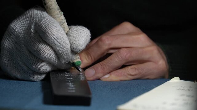 Worker wearing gloves hand engraving metal inscription with precision tools