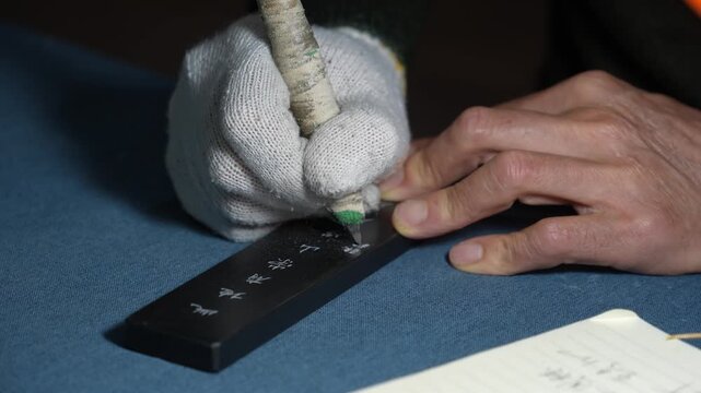 craftsman wearing gloves holding carving knife engraving on wooden board