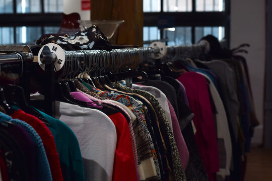 Rows of clothing hanging on racks inside a thrift store, showing second hand fashion, retail shopping, and organized garment displays