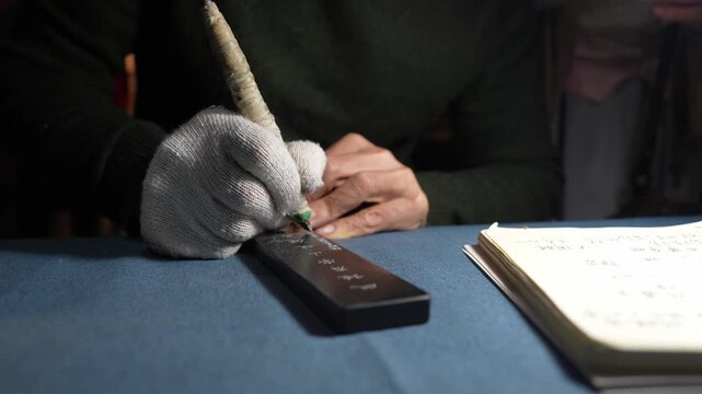 Artisan wearing gloves holding a brush to write Chinese calligraphy characters