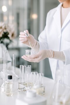 Laboratory technician transferring oil droplet with dropper into beaker for cosmetic testing and product formulation use
