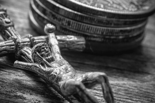 Vintage crucifix with Jesus Christ figure beside stacked old coins