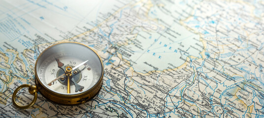 Vintage brass compass on an old geographic map close up. Antique navigation instrument for travel, exploration, geography and discovery concept. Adventure, tourism, cartography and orientation theme. © Tryfonov