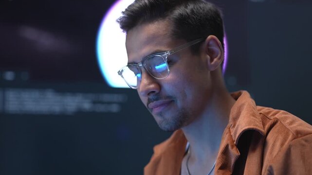 Close up portrait of a focused Asian businessman wearing glasses while tracking core database structures during a late-night software development session.