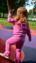 Fototapeta premium Toddler girl walking and balancing on colorful playground surface in sunny outdoor park. Active childhood, coordination training and playful exploration concept with modern recreational equipment.