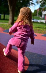 Fototapeta premium Toddler girl walking and balancing on colorful playground surface in sunny outdoor park. Active childhood, coordination training and playful exploration concept with modern recreational equipment.