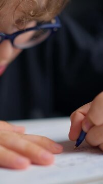 Close-up images of a young child with glasses concentrating while writing with a pen on paper, demonstrating focused learning and engagement in a writing activity indoors