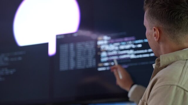 Over the shoulder view of tech developers analyzing software coding lines and circuit architectures across dual monitor desktop screens in a startup office.