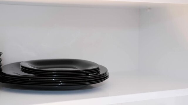 Woman Hand Organizing Black Plates in Kitchen Cabinet, Close Up of Housewife Putting Dishes on Shelf, Kitchen Storage and Organization Concept