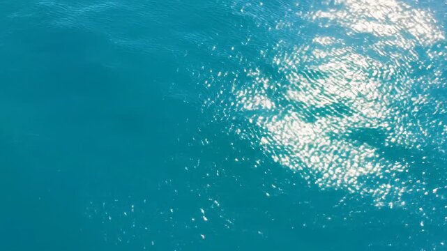 Extreme 90-degree top-down aerial video of crystal-clear, vibrant blue water with shimmering ripple patterns, illuminated by golden hour light, emphasizing organic abstract light and shadow,