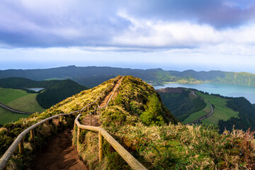 Dramatic wooden-railed footpath ascending along a volcanic ridge in the Azores with sweeping views of a crater lake and the Atlantic Ocean below. © Jelena
