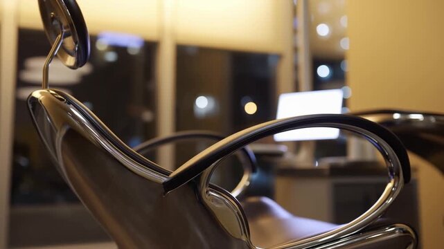 Pan slow motion tracking shot of salon chair facing illuminated workstation and mirror in modern interior at night
