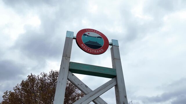 Looking up at the logo of the public beach in Zam&aacute;rdi, Hungary. Cloudy autumn day at the Lake Balaton. Slow motion panning view with quiet, off season atmosphere.