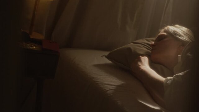 Handheld shot of blonde gen Z woman waking up, checking smartphone and continuing to sleep in bed during slow weekend morning