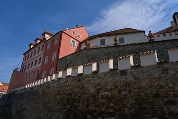 Pisek, Czech Republic - April 18, 2026 - Historic castle walls and pink building under a bright blue sky © Ivo