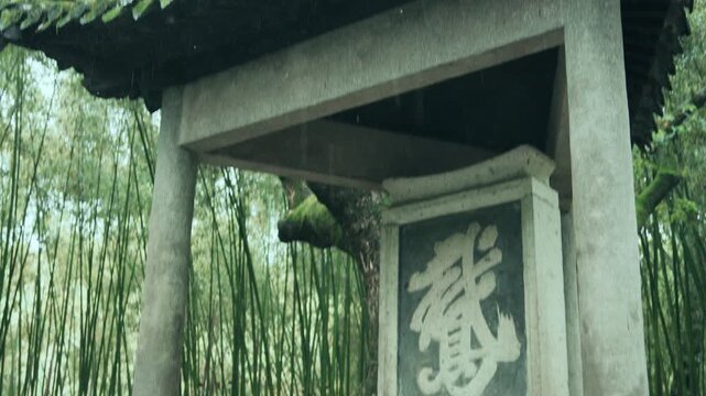 Traditional Chinese stone pavilion with calligraphy surrounded by green bamboo forest