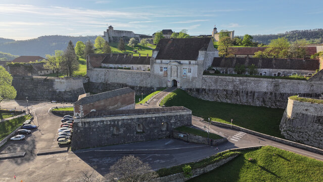 Aerial view of the historic Besancon Citadel featuring massive stone fortifications, a central gatehouse, and lush green slopes under a clear sky in Besancon, Bourgogne-Franche-Comte, France.