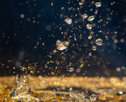 Water droplets create splashes in golden liquid with bright reflections during daytime