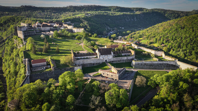 Aerial view of the historic Besancon Citadel with its massive stone fortifications and lush green hills under bright sunlight in Besancon, Bourgogne-Franche-Comte, France.