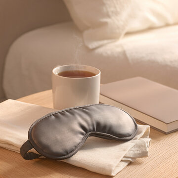 Relaxing sleep mask beside warm tea on bedside table