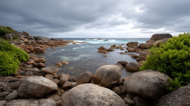 A dramatic and moody seascape featuring rugged coastal rocks under a dark overcast sky