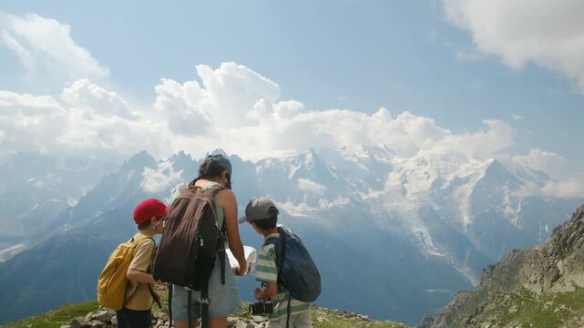Mother with two sons hiking in the mountains, stopping to check the map and admire the amazing panoramic view of the majestic mont blanc massif on a sunny day
