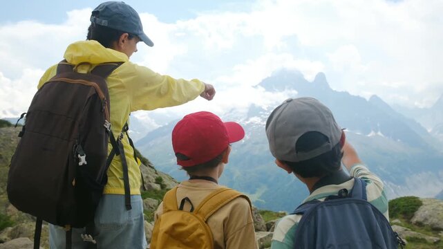 Adventurous family of hikers pointing at the stunning mountain peak scenery during a summer trek, sharing a moment of discovery and exploration in the great outdoors