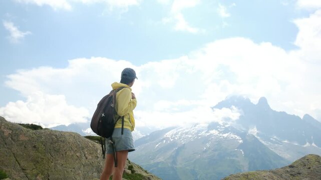 Hiker woman with a backpack standing on a mountain summit looking at the scenic alpine landscape of mont blanc, embodying freedom, adventure, and exploration