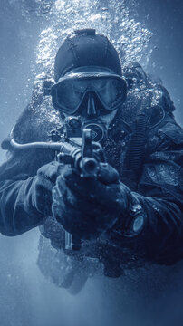 Underwater tactical military diver swimming in deep blue water holding an automatic rifle and wearing professional scuba gear with diving mask and oxygen tank for dangerous secret mission