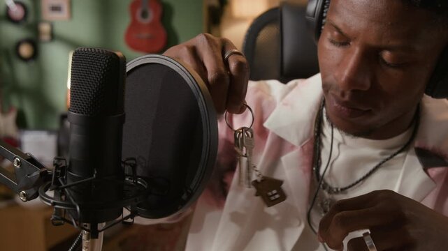 Close up shot of young adult Black male Foley artist jingling keys near microphone recording realistic sound effects in home based studio