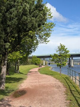 Drammenselva River waterfront in Drammen, Norway. City buildings on forested hill, bridge and urban landscape under blue sky with cloud
