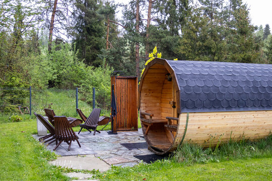Outdoor wooden hot tub standing near forest cabin during rainy spring day in mountains of Poland. Cozy countryside spa retreat with steaming water, wellness atmosphere and peaceful nature views.