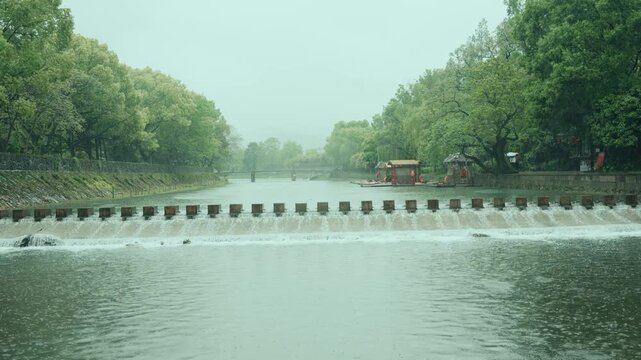 Misty view of the Su Causeway weir in Hangzhou West Lake with lush green trees and flowing water