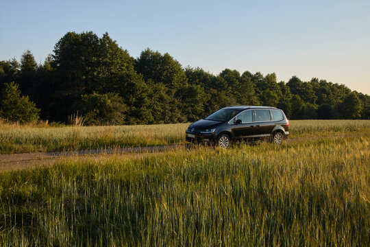 The Volkswagen Sharan is parked on a dirt road next to a tall grass field during sunset with trees lining the horizon. Zory, Poland 03.07.2015